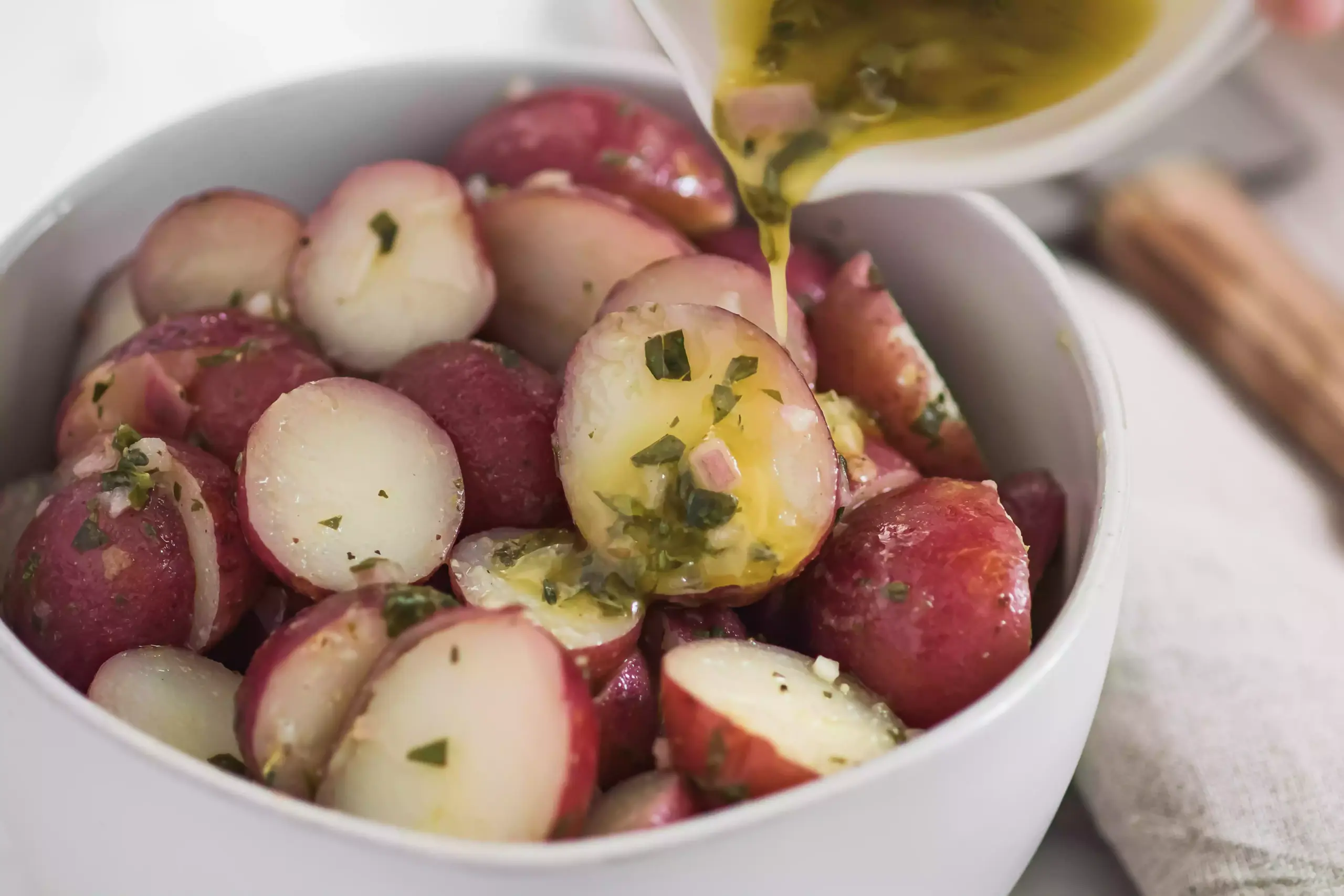 Ajouter de la viniagrette dans un bol de pommes de terre rouges coupées en deux pour une recette de salade niçoise.